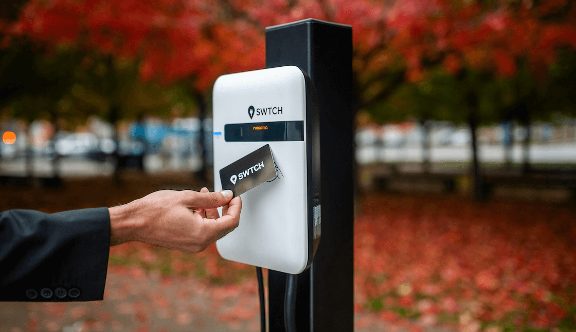A hand holding an RFID access and payment card up to a reader on a level 2 EV charger