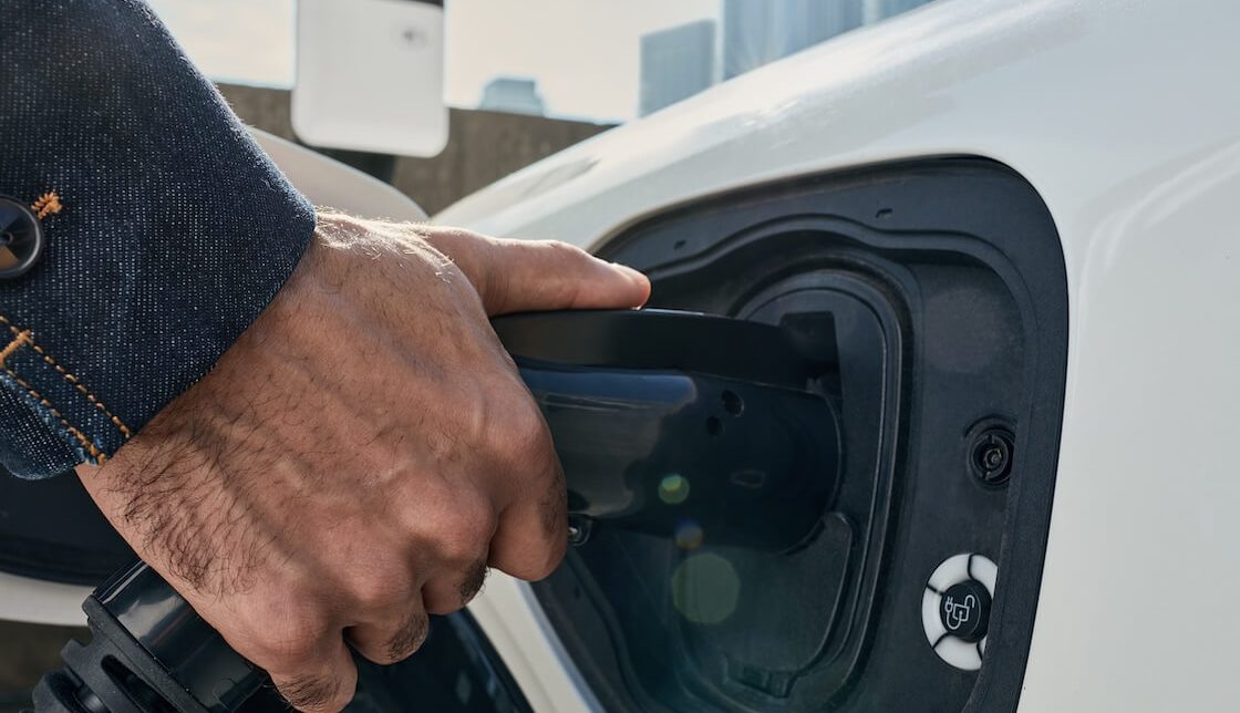 Demonstrates a man plugging an EV charger connector into his vehicle